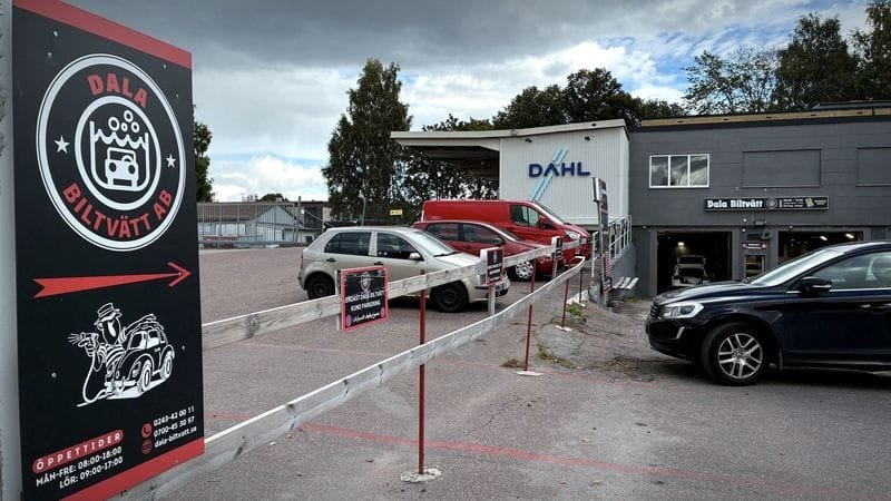 Dala Biltvätts skylt med logotypen och en pil som visar vägen in, framför parkeringen och lokalen.